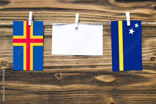 Hanging flags of Aland Islands and Curacao attached to rope with clothes pins with copy space on white note paper on wooden background.Diplomatic relations between countries. photo