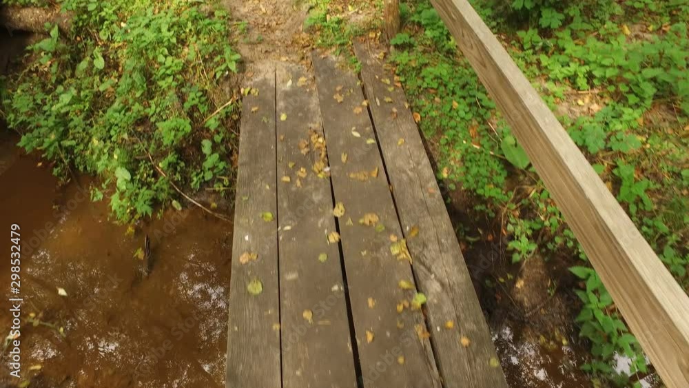 Movement on small wooden bridge consisting of boards through shallow forest stream Movement on small wooden bridge consisting of boards through shallow forest stream