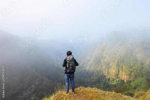 A backpack man standing on cliff and see over view in nature.Tourist  enjoying fresh air. A man enjoying free happiness in beautiful Thailand landscape. © Teerayut