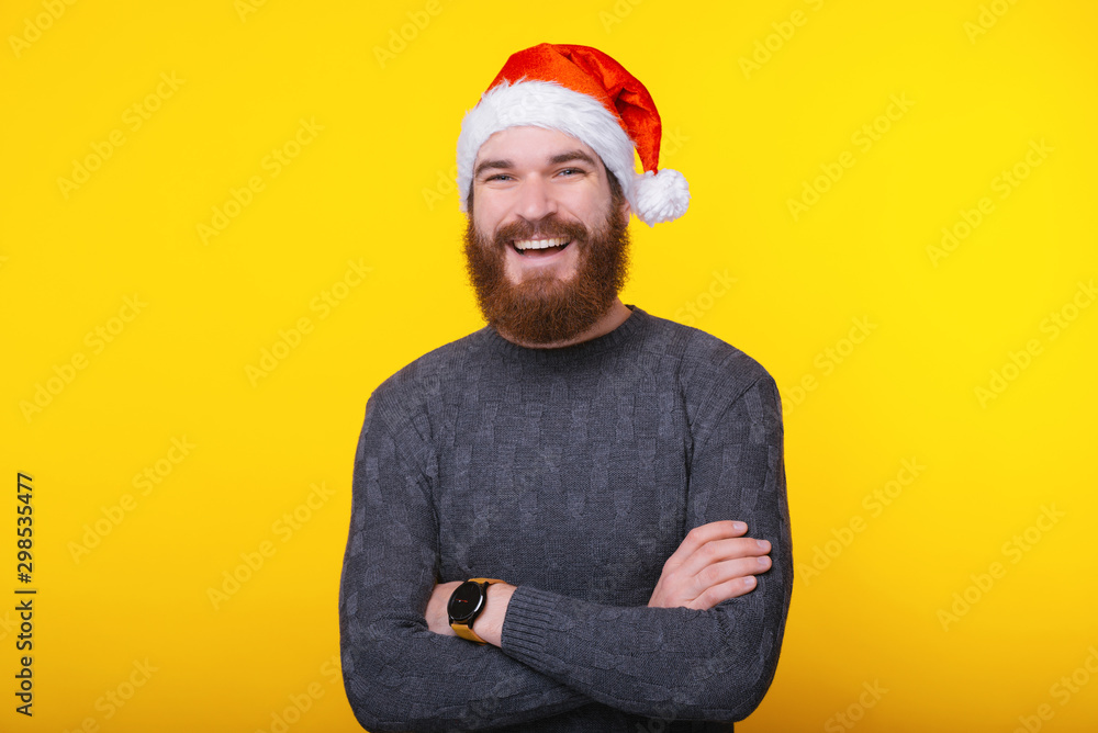 Portrait of young smiling man wearing santa claus hat with crossed arms looking confident at the camera
