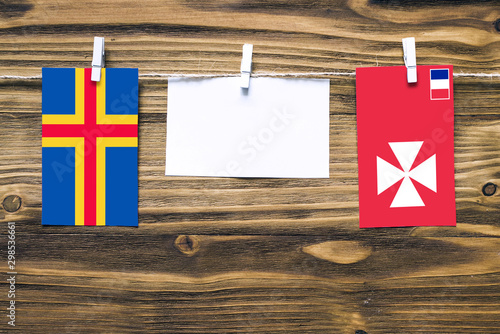 Hanging flags of Aland Islands and Wallis And Futuna attached to rope with clothes pins with copy space on white note paper on wooden background.Diplomatic relations between countries. photo