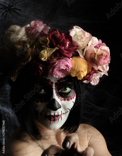 girl with black hair is dressed in a wreath of multi-colored roses and makeup is made on her face Sugar skull