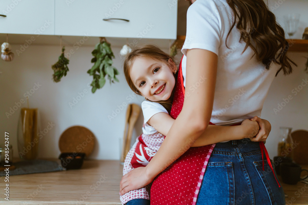 daughter hugs mom at the waist in the kitchen daughter hugs mom at the waist in the kitchen