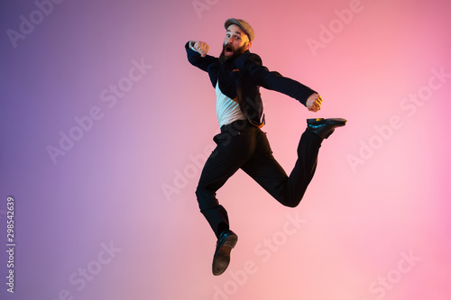 Full length portrait of happy jumping man wearing office clothes in neon light isolated on gradient background. Emotions, ad concept. Calling, hurrying up, office work or sale, shopping. Copyspace. © master1305