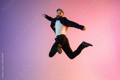 Full length portrait of happy jumping man wearing office clothes in neon light isolated on gradient background. Emotions, ad concept. Calling, hurrying up, office work or sale, shopping. Copyspace.