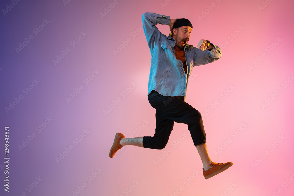 Full length portrait of happy jumping man wearing casual clothes in neon light isolated on gradient background. Emotions, ad concept. Expressive hurrying up, late for work or sale, shopping. - obrazy, fototapety, plakaty 