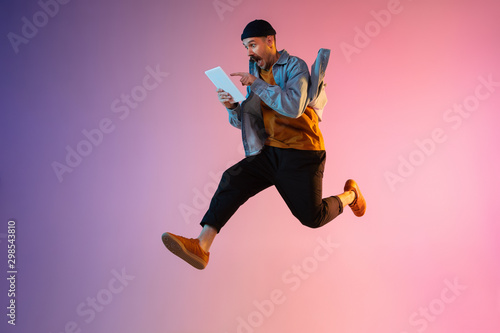 Fotografia Full length portrait of happy jumping man wearing casual clothes in neon light isolated on gradient background
