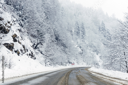 Snowy road scene in winter, with snowy trees, rocks and asphalt road. © ardasavasciogullari