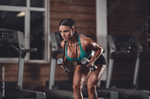Photo of athletic young girl doing a fitness workout with dumbbells in the gym