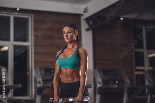 Photo of athletic young girl doing a fitness workout with dumbbells in the gym
