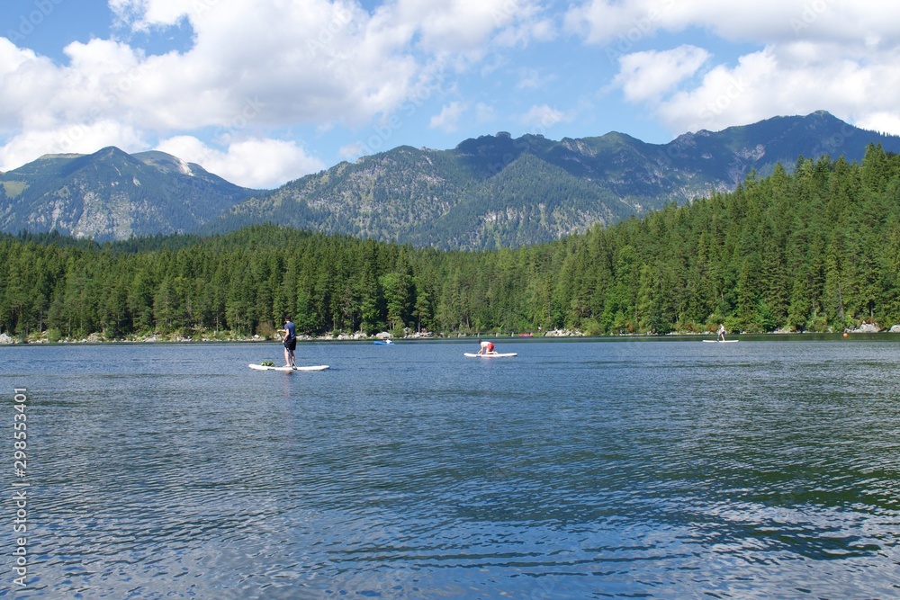 People Paddle Boarding in Lake with forrest and mountains
