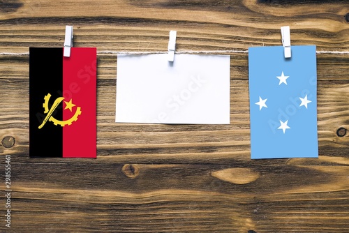 Hanging flags of Angola and Micronesia attached to rope with clothes pins with copy space on white note paper on wooden background.Diplomatic relations between countries. photo