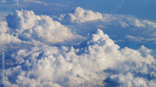 Fototapeta Naklejka Na Ścianę i Meble -  Flying over heavenly beautiful cloudscape. Picturesque panorama of dense fluffy clouds softly lit by the sun, moving from right to left on the clear blue sky. View from the airplane window.