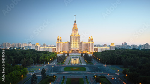 Motion of Moscow State University in the evening, aerial view. Camera moving towards MSU, showing also its alleys and outdoor lighting gradually turning on.