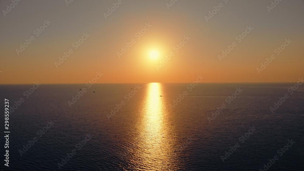 Beautiful aerial panorama of the sunset sea. Picturesque view to the sun going down over the sea, leaving a light path over the water, and the boat crossing the light path in front of the sun.