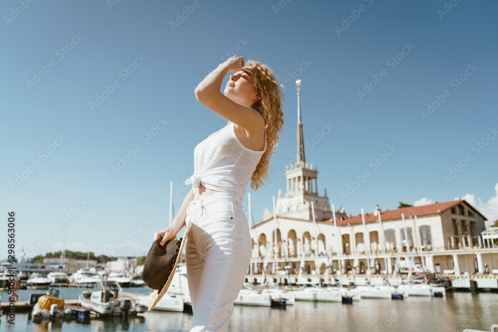 girl looks into the distance with her hand covering her eyes from the sun against the background of the seaport