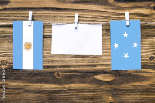 Hanging flags of Argentina and Micronesia attached to rope with clothes pins with copy space on white note paper on wooden background.Diplomatic relations between countries. photo