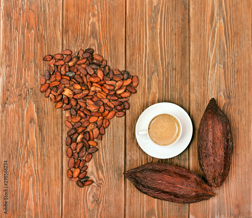 South America continent made of cocoa beans and cocoa pods with cup of cacao drink on wooden background. Top view.