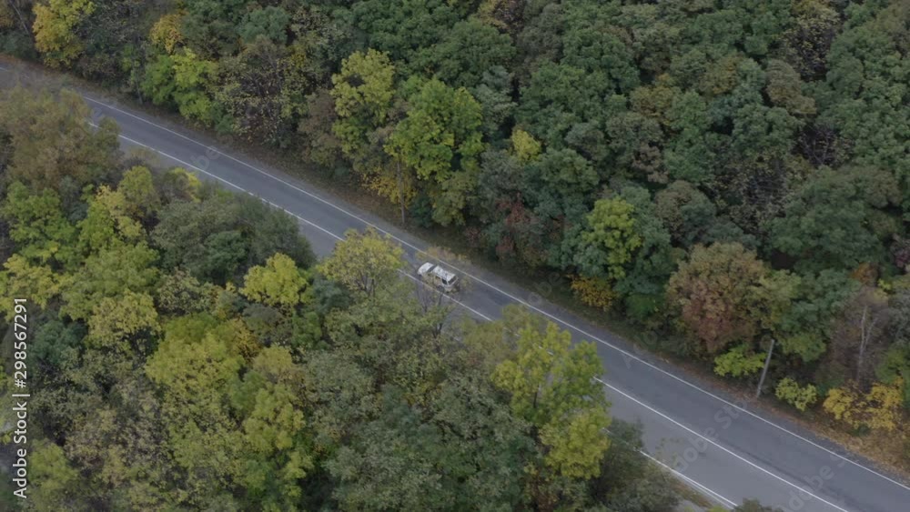 Car passing on a two lane road in the midst of autumn forest with different green hues tree leaves. Car passing on a two lane road in the midst of autumn forest with different green hues tree leaves.