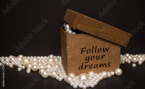 Follow yur dreams wooden box filled up and surrounded with the white pearls on the black background. photo