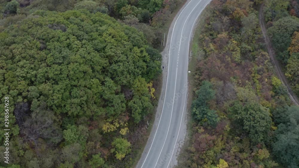 Empty two lanes asphalt road with in the autumn forest with colorful autumn tree leaves. Aerial shot. Empty two lanes asphalt road with in the autumn forest with colorful autumn tree leaves. Aerial shot.