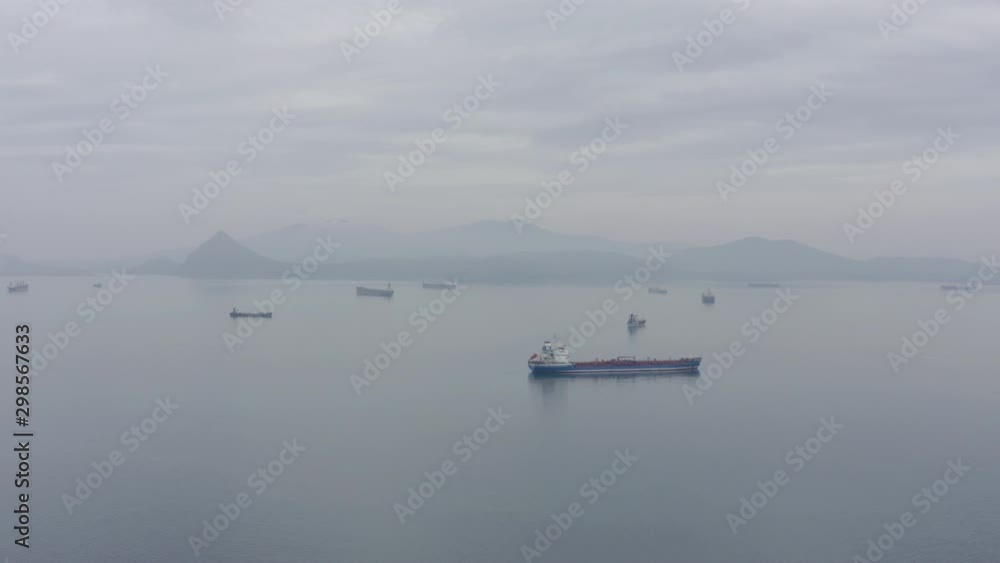 Ships at anchorage waiting area in a calm weather, with mountain ridge in far distance on the overcast day. Aerial shot Ships at anchorage waiting area in a calm weather, with mountain ridge in far distance on the overcast day. Aerial shot