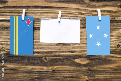 Hanging flags of Aruba and Micronesia attached to rope with clothes pins with copy space on white note paper on wooden background.Diplomatic relations between countries. photo