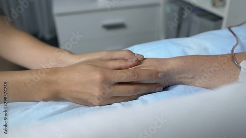 Caring daughter holding hand of terminally ill mother with chemotherapy dropper