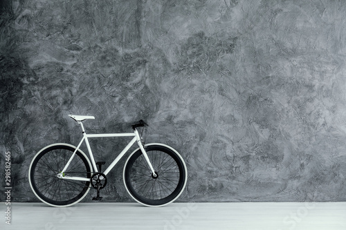White and black bike on empty grey concrete wall, real photo with copy space
