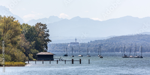 LAKE AMMERSEE, BAVARIA / GERMANY - Sept 29, 2019: Panorama view of landscape at Lake Ammersee: a dock, a boat house, sail boats anchoring. Far in the distance the alps and the Marienmünster Dießen. photo
