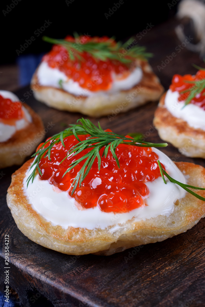 Pancakes with red caviar and cream cheese topped with dill on the wooden board Pancakes with red caviar and cream cheese topped with dill on the wooden board