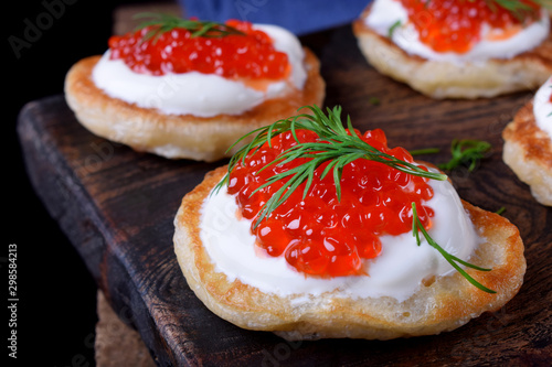 Pancakes with red caviar and cream cheese topped with dill on the wooden board