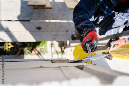 Construction worker plastering a wall with trowel cement mortar applying adhesive cement on the Autoclaved aerated concrete AAC brick high angle close up on hand holding the tool outdoor