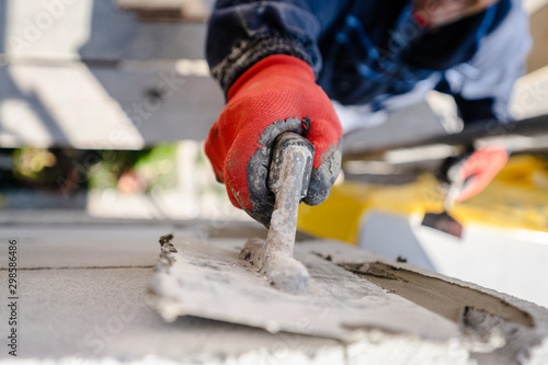 Construction worker plastering a wall with trowel cement mortar applying adhesive cement on the Autoclaved aerated concrete AAC brick high angle close up on hand holding the tool outdoor photo