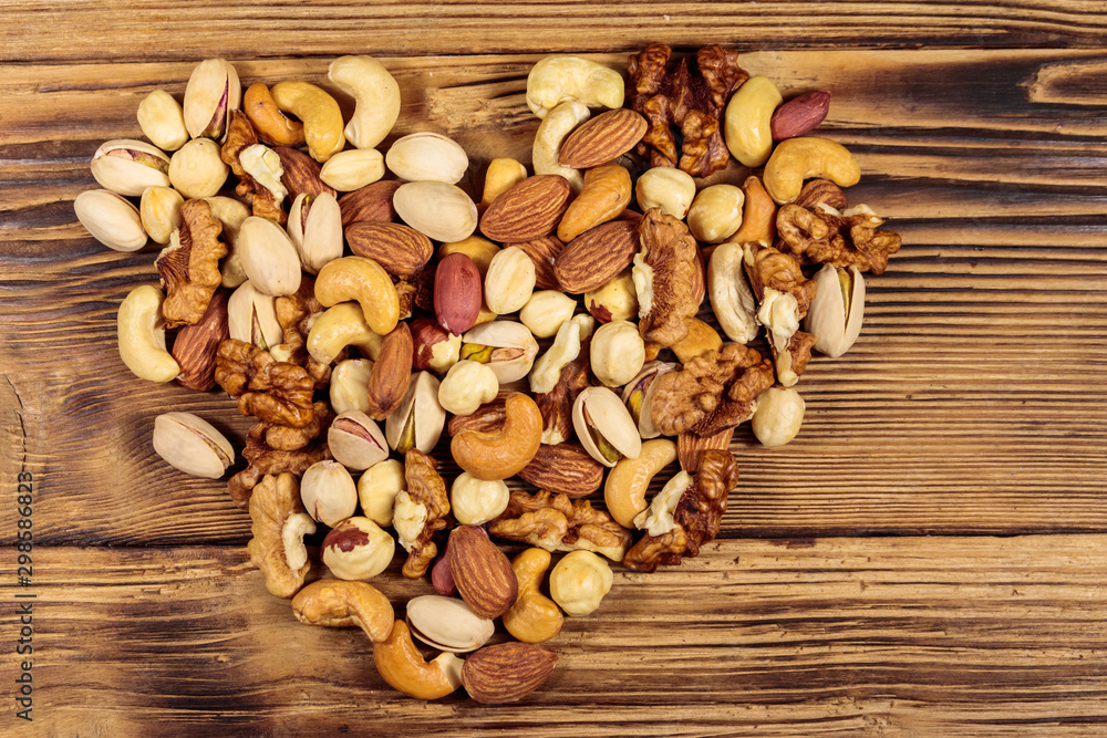 Pile of mixed nuts in shape of heart on wooden table. Top view. Walnuts, pistachio, almond, peanut, cashew, hazelnut on wood background. Healthy eating concept Pile of mixed nuts in shape of heart on wooden table. Top view. Walnuts, pistachio, almond, peanut, cashew, hazelnut on wood background. Healthy eating concept