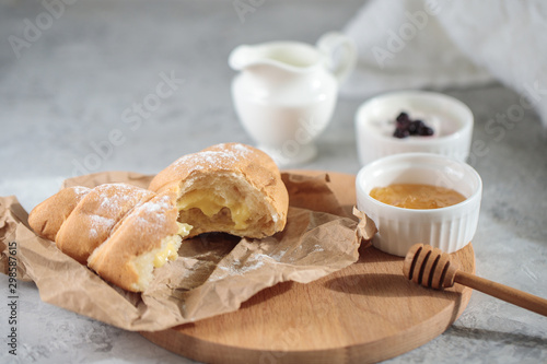 Delicious breakfast concept, close-up. A broken croissant with cream lies on a wooden board, with a honey bowl and a jug of cream.