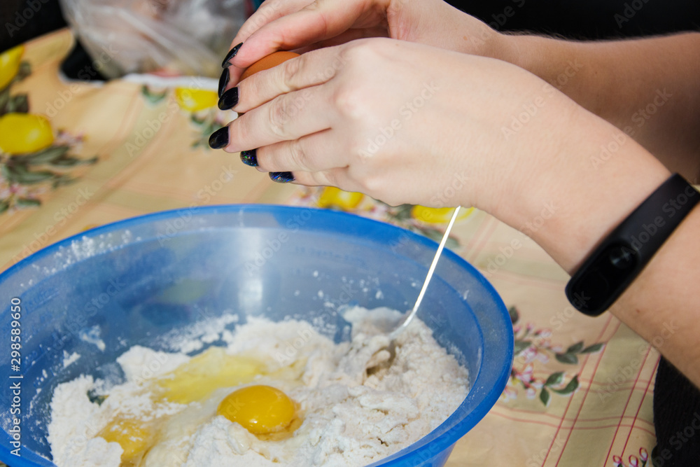 Woman with black manicure cooking and breaking eggs into a blue bowl of flour to make dough. Woman with black manicure cooking and breaking eggs into a blue bowl of flour to make dough.