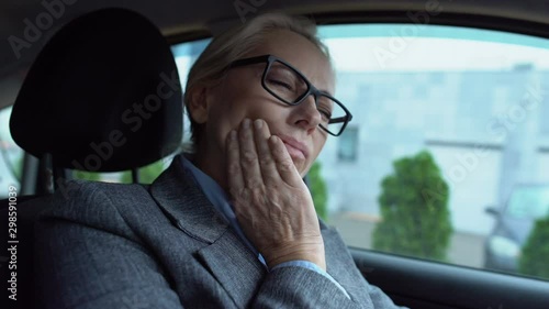 Mature woman feeling toothpain sitting in car, gum sensitivity caries prevention