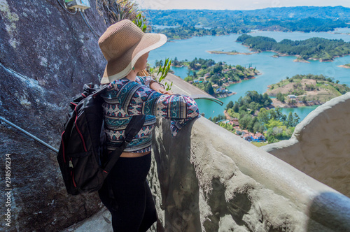 Vista trasera de mujer turista contemplando la naturaleza en Guatape Colombia desde la cima de la piedra del peñol photo