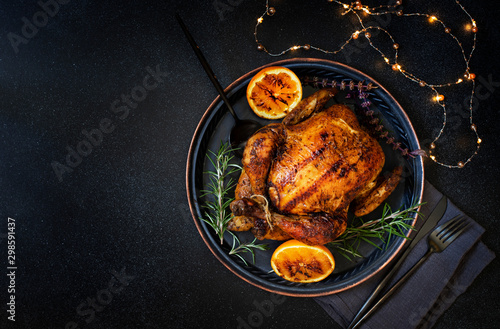 Baked whole chicken with oranges and rosemary. Tray with a festive Christmas dish on a black background. Top view, flatlay. Copyspace