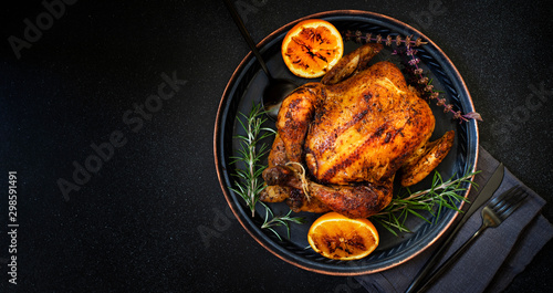 Baked whole chicken with oranges and rosemary. Tray with a festive Christmas dish on a black background. Top view, flatlay. Copyspace