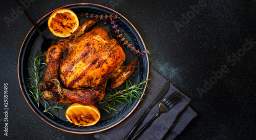 Baked whole chicken with oranges and rosemary. Tray with a festive Christmas dish on a black background. Top view, flatlay. Copyspace photo