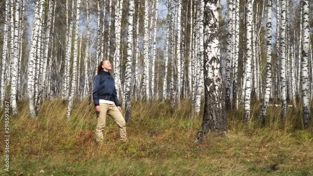 Young Caucasian Woman Enjoying Fresh Air in Birch Grove in Autumn. Female Traveler Breathing Deeply in Colorful Yellow Leaf-Bearing Deciduous Fall Forest Young Caucasian Woman Enjoying Fresh Air in Birch Grove in Autumn. Female Traveler Breathing Deeply in Colorful Yellow Leaf-Bearing Deciduous Fall Forest