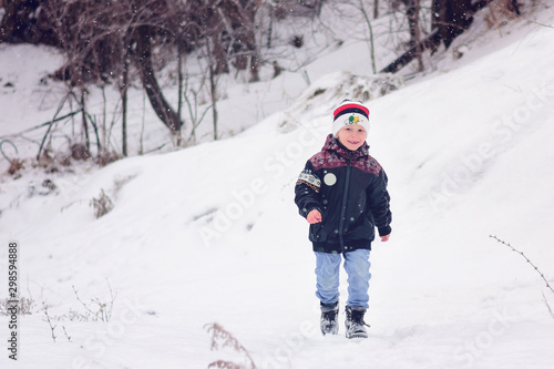 Little smiling boy plays and runs on the street in snowy winter