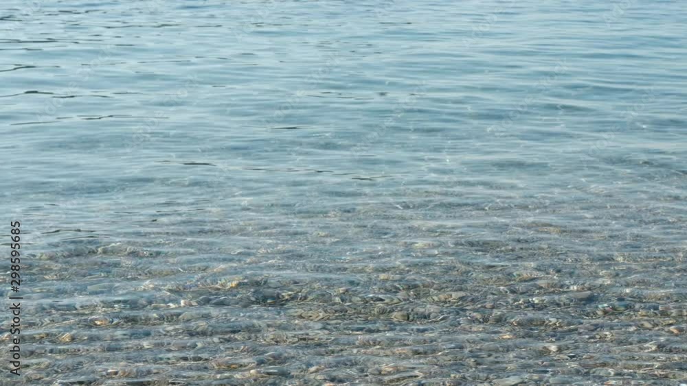 Sea water surface at the pebble beach. Beautiful sun beams in ripple waves. Sea water surface at the pebble beach. Beautiful sun beams in ripple waves.