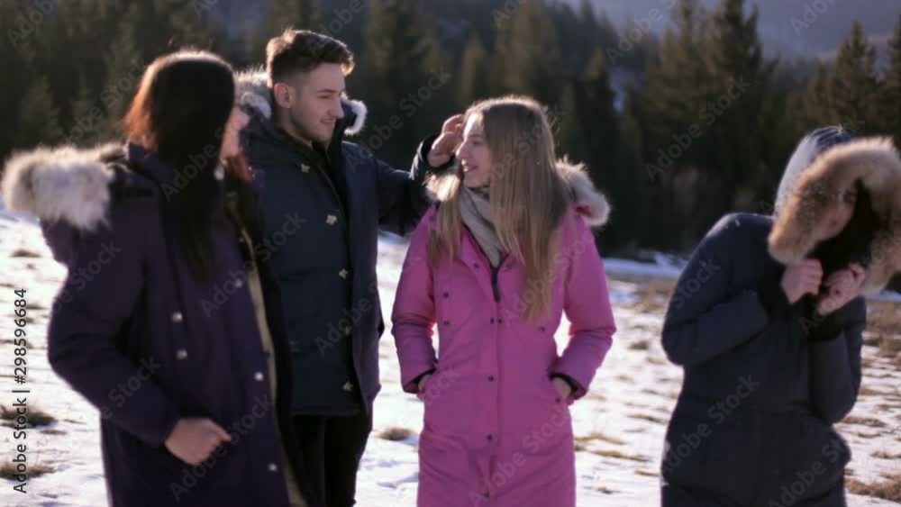 Three girls and a guy have a rest in the mountains against the background of a coniferous forest on a sunny winter day Three girls and a guy have a rest in the mountains against the background of a coniferous forest on a sunny winter day