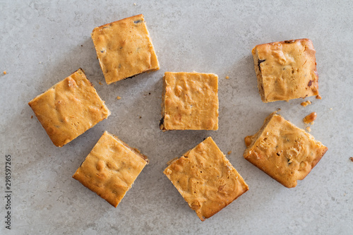 Homemade blondie brownie squares with white chocolate and peanut butter scattered on grey stone background, top view flat lay