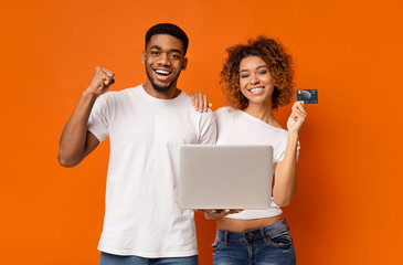 Cheerful african couple shopping online on laptop with bank card