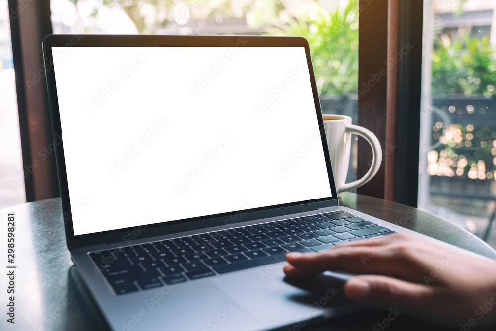Mockup image of a hand using and touching on laptop touchpad with blank white desktop screen with coffee cup on the table Mockup image of a hand using and touching on laptop touchpad with blank white desktop screen with coffee cup on the table