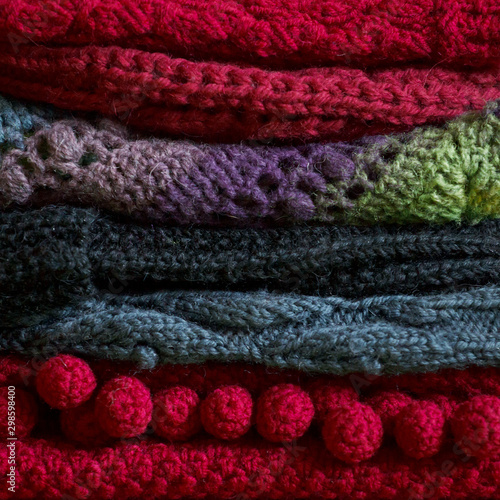 Bunch of knitted warm bright sweaters with different knitting patterns folded in stack  clearly visible texture. Stylish fall winter seasonal knitwear clothing. Closeup  copy space